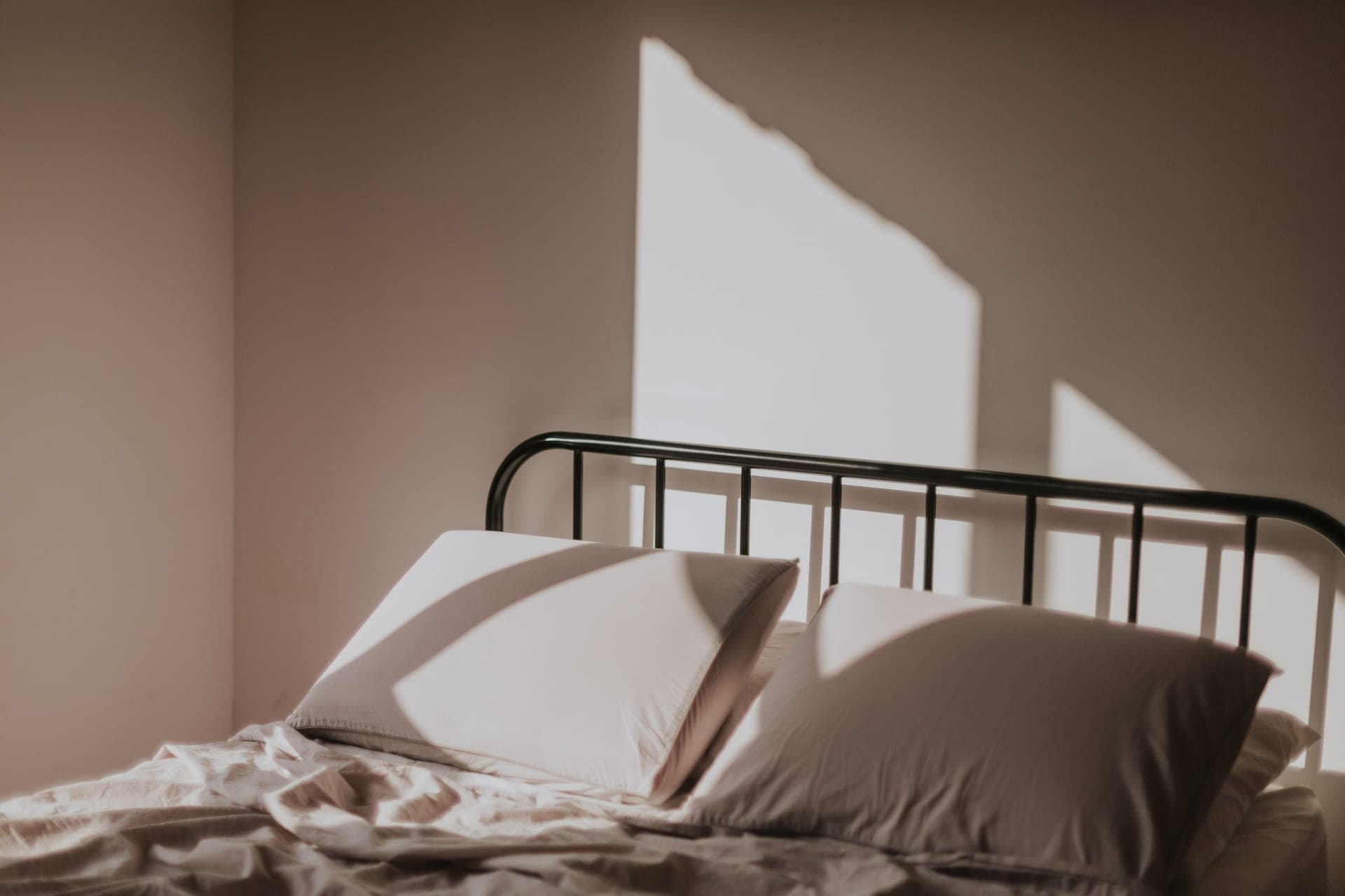 A neatly made bed with a metal headboard in soft morning light