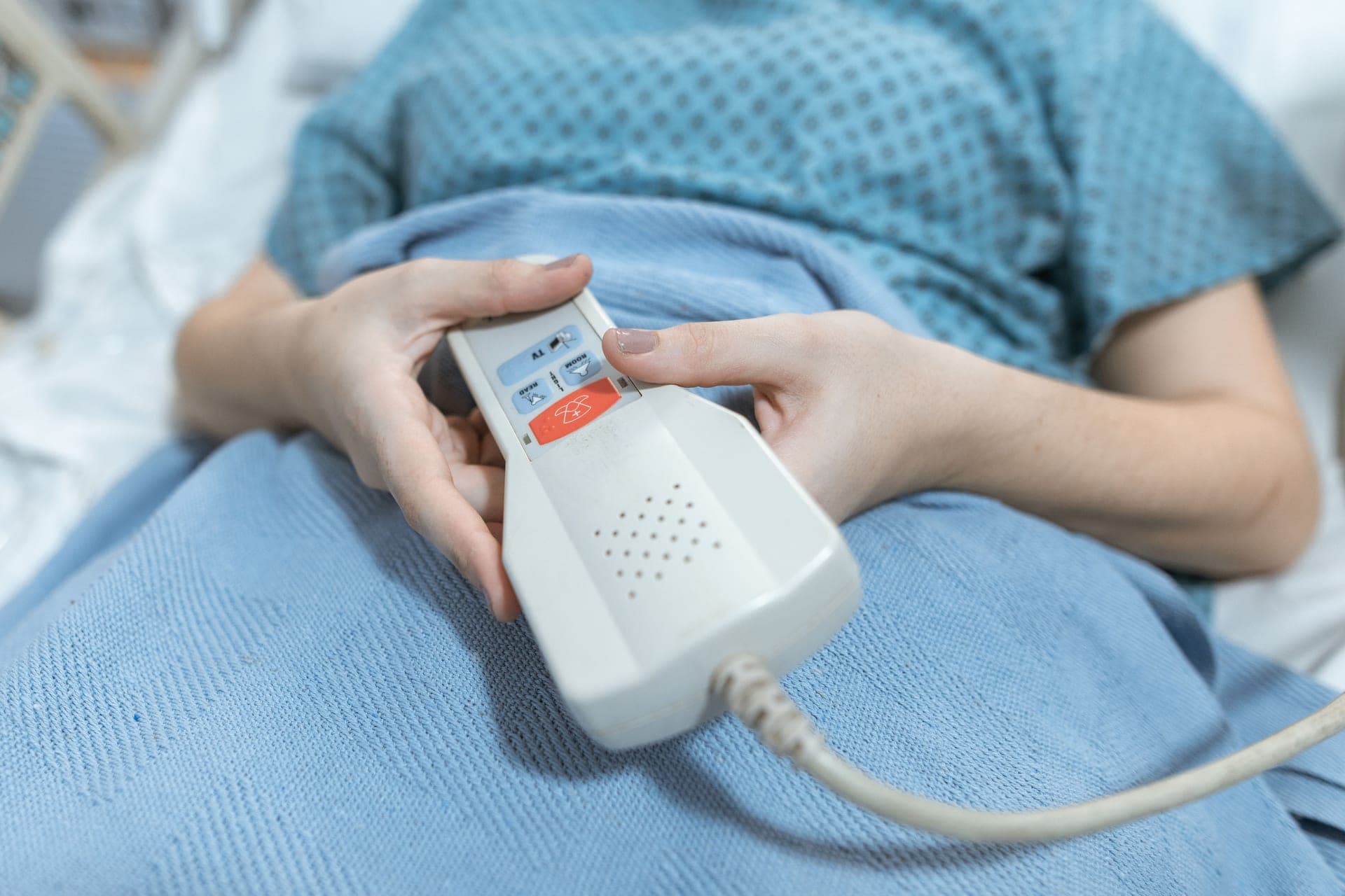 A hand holding a white corded remote control in bed