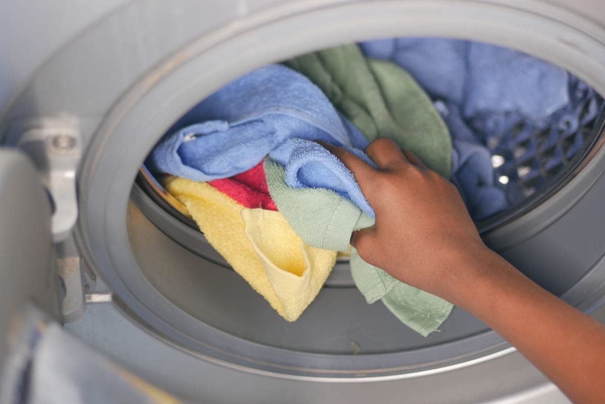 Hands loading laundry into a washing machine