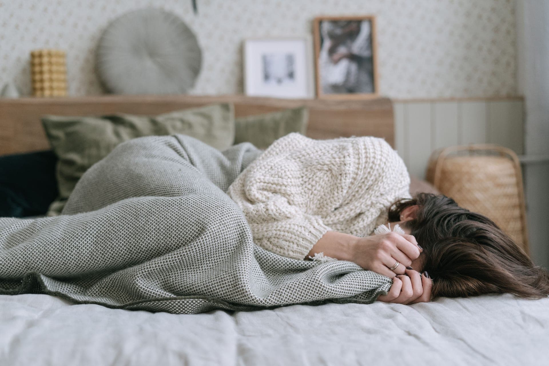 A person curled under a textured blanket on a made bed