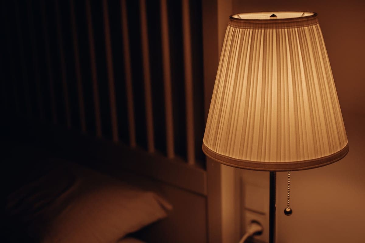 A bedside lamp on a nightstand in a dark bedroom