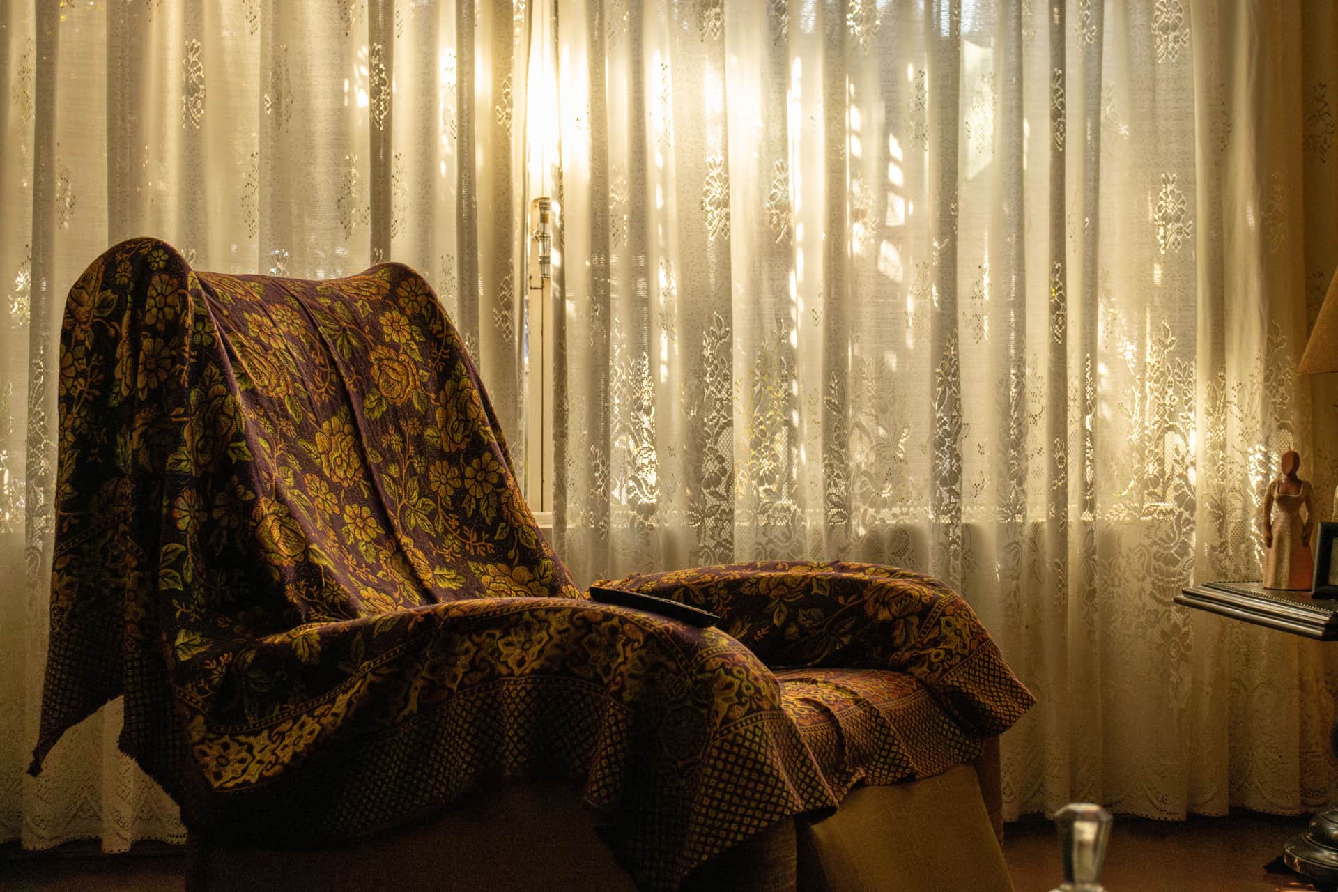 A heavy patterned throw draped over an armchair by a curtained window