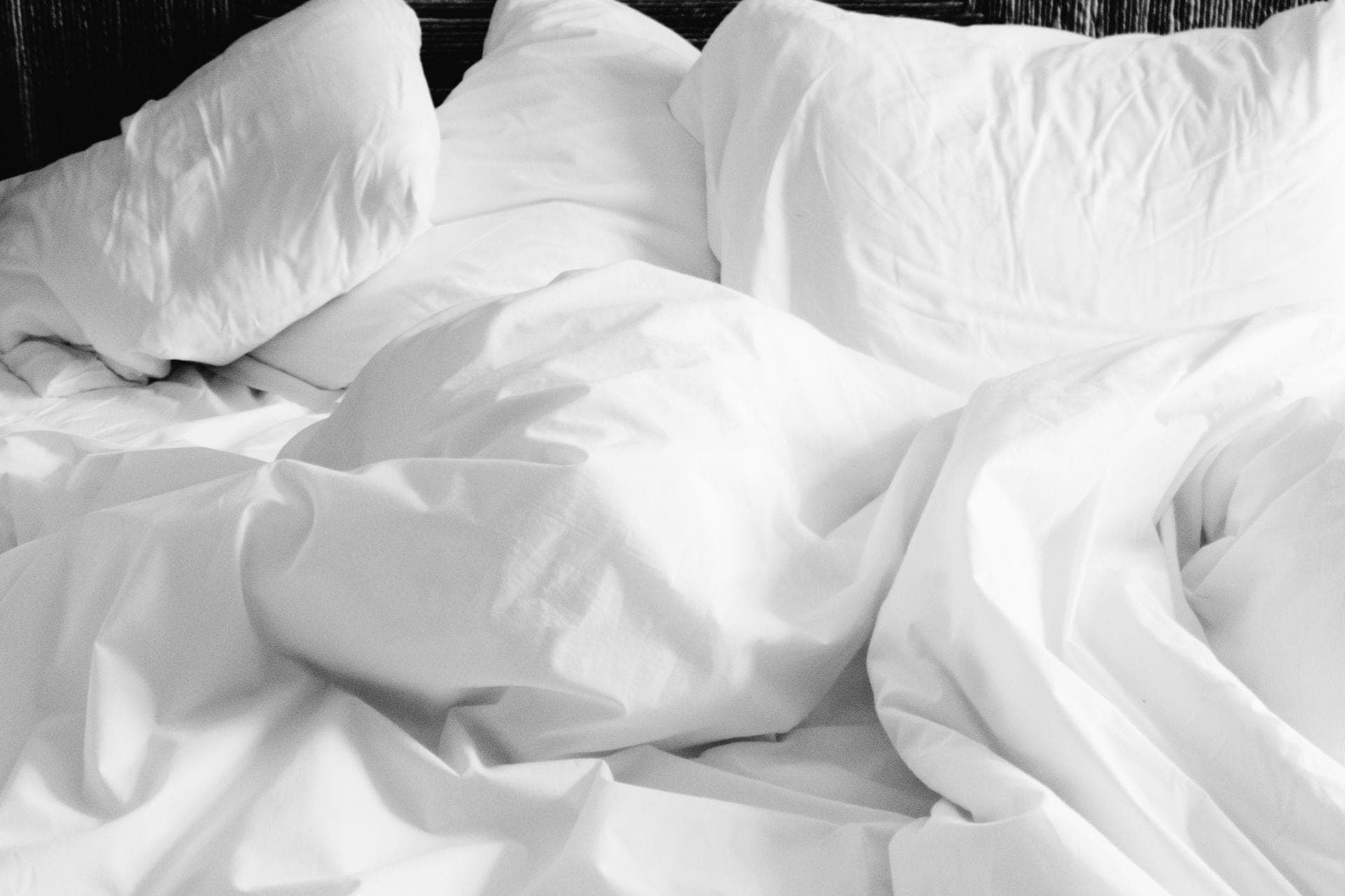 A made bed with soft white sheets in a bright bedroom