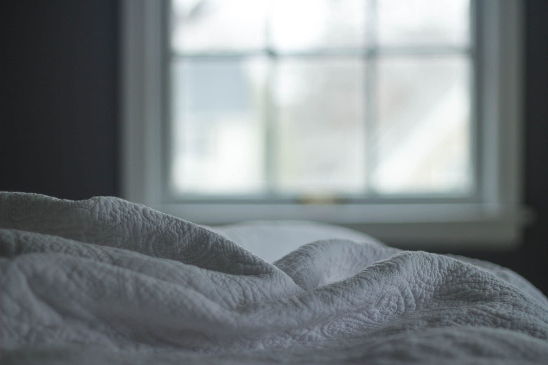 A quilted blanket on a made bed beside a window in morning light