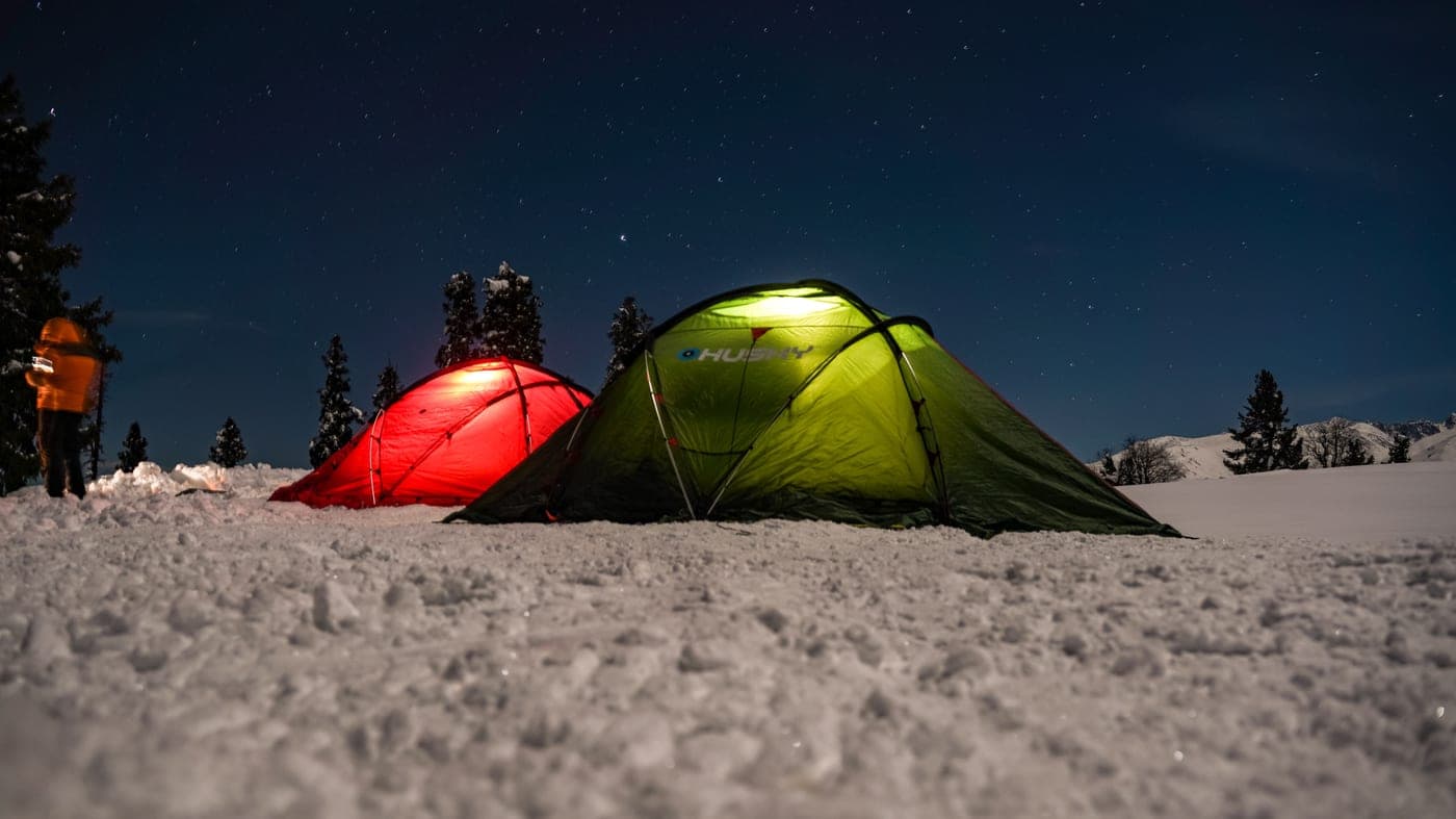 A tent lit from within at night, on cold ground